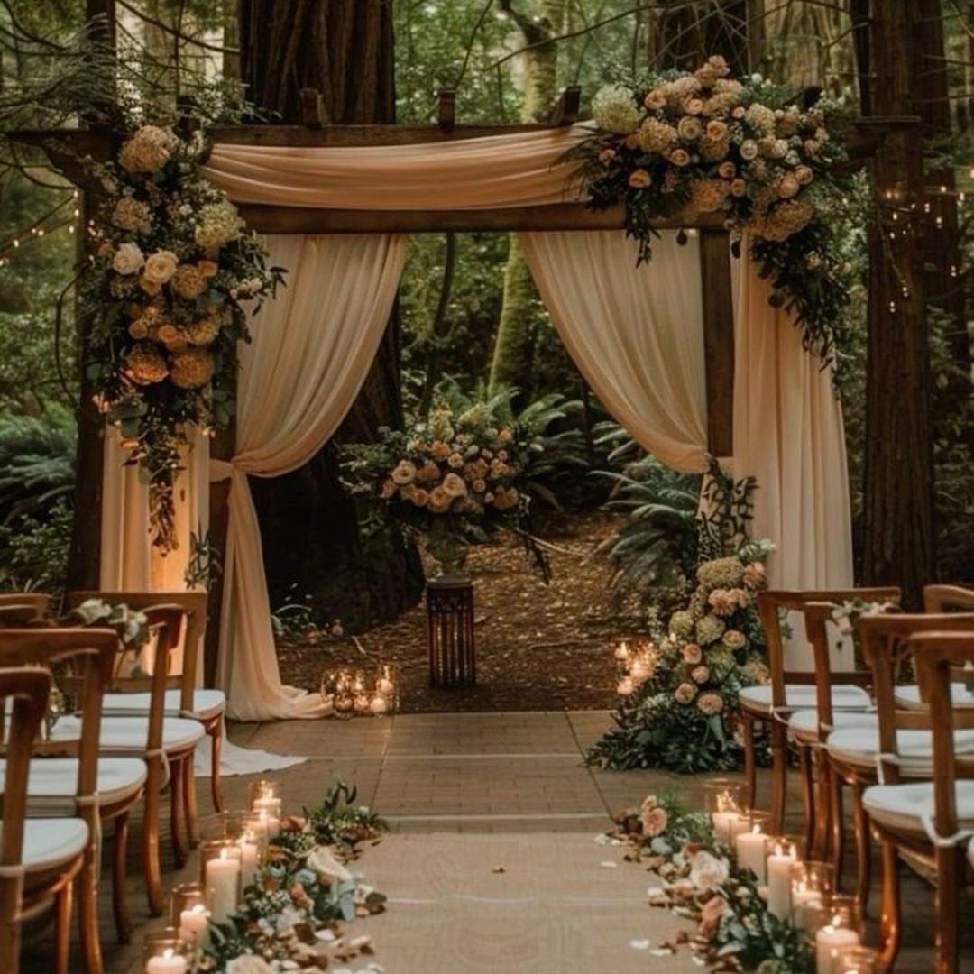 Candlelit wedding aisle leading to a draped floral arch in a redwood forest
