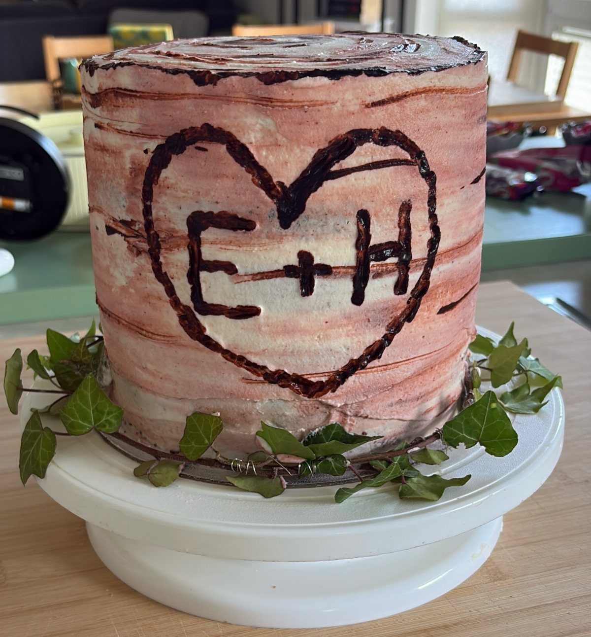 Tree trunk wedding cake with a carved heart and green ivy leaves.