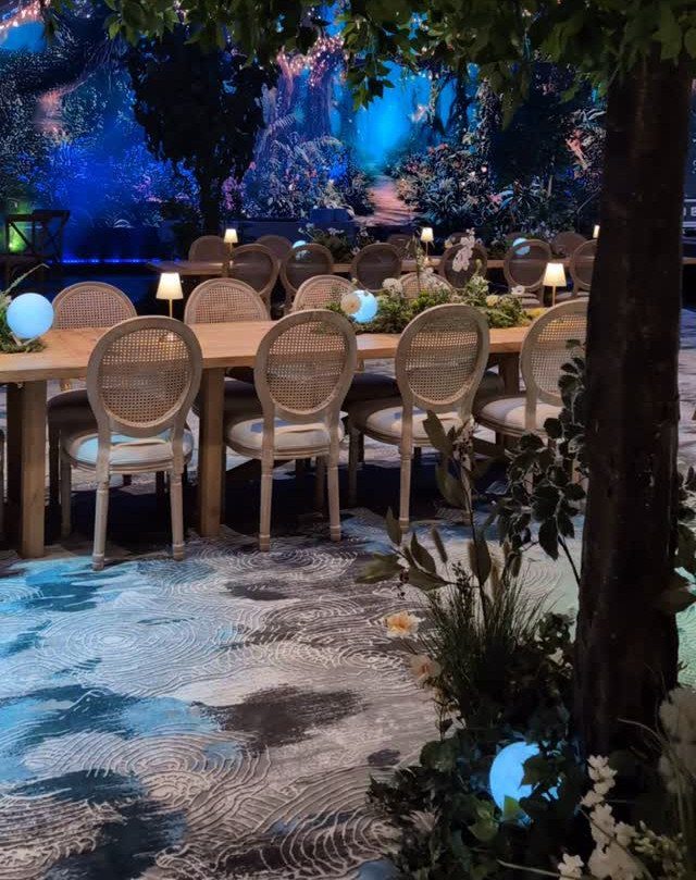 Wooden dining table with cane chairs in a blue-lit enchanted forest setting