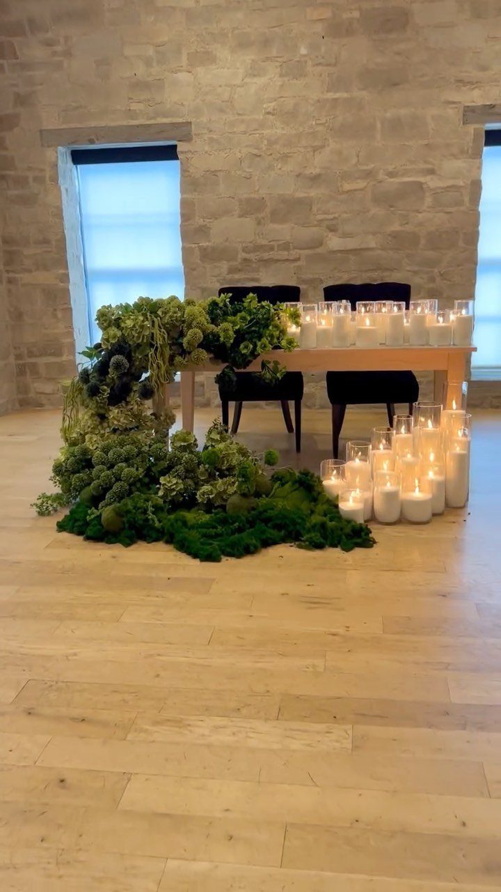 Moss and greenery arrangement flowing from a wooden table with glowing white candles.