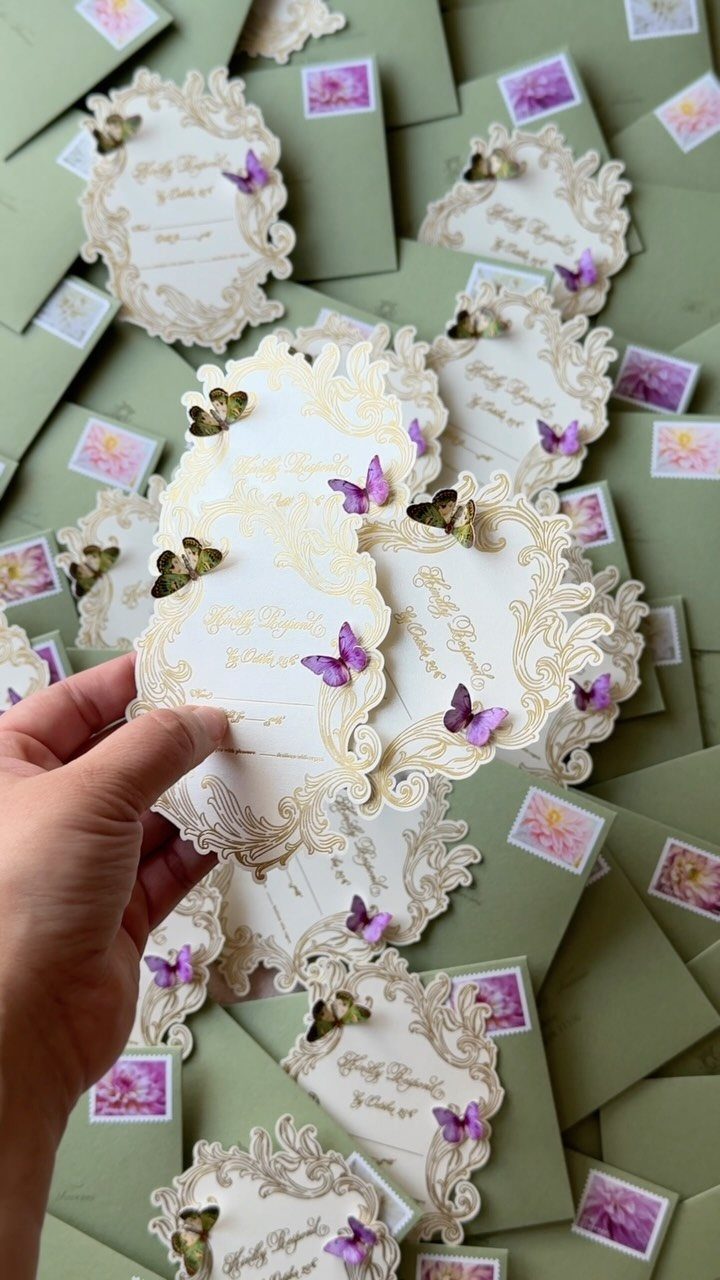 Ornate cream wedding invitations with butterfly accents and sage green envelopes.