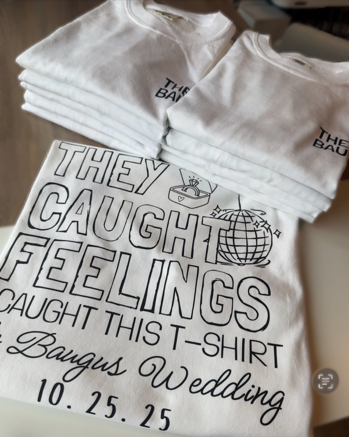 White custom t-shirts announcing a wedding with black text and ring illustration.