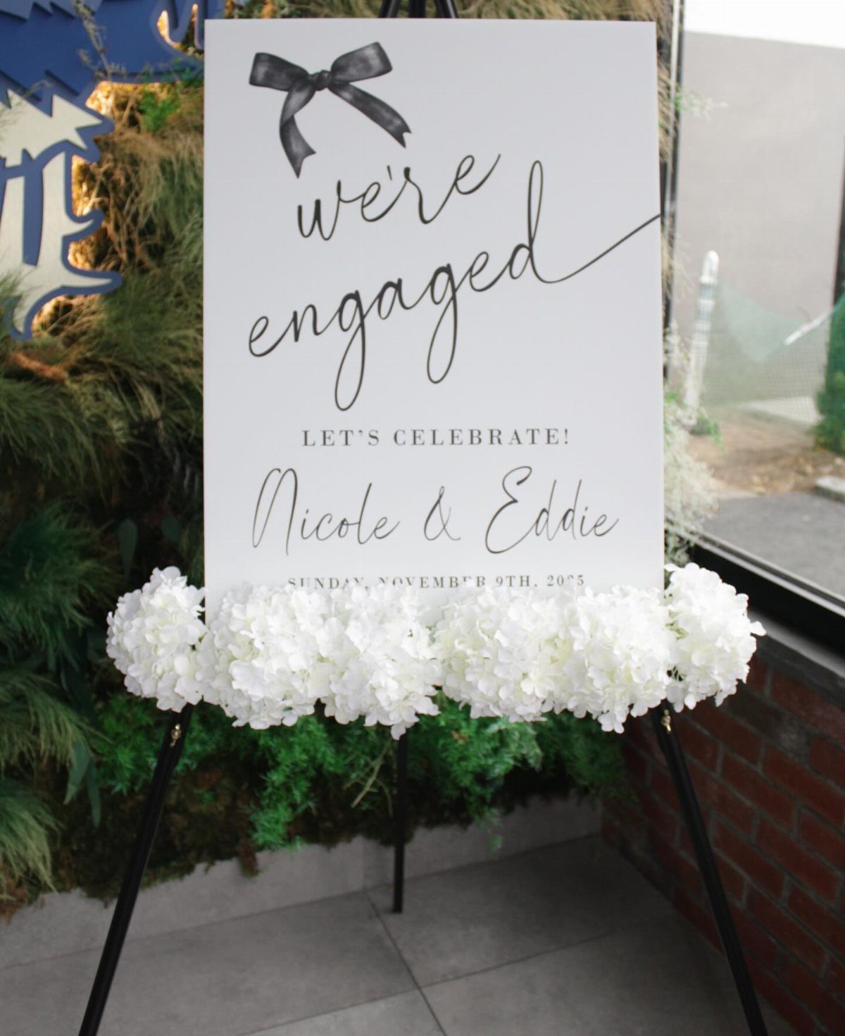 Engagement announcement sign on an easel decorated with white hydrangea flowers