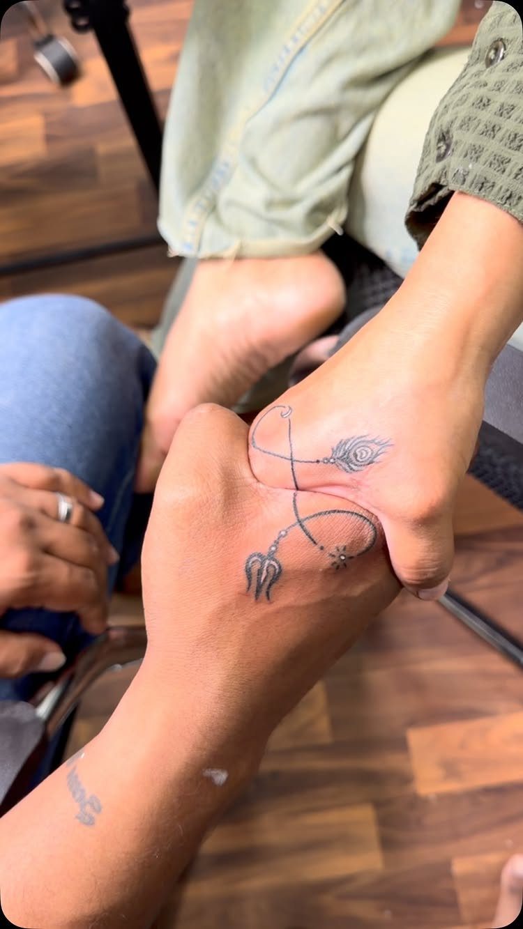 Two feet positioned together showing matching black ink tattoos that form one design.