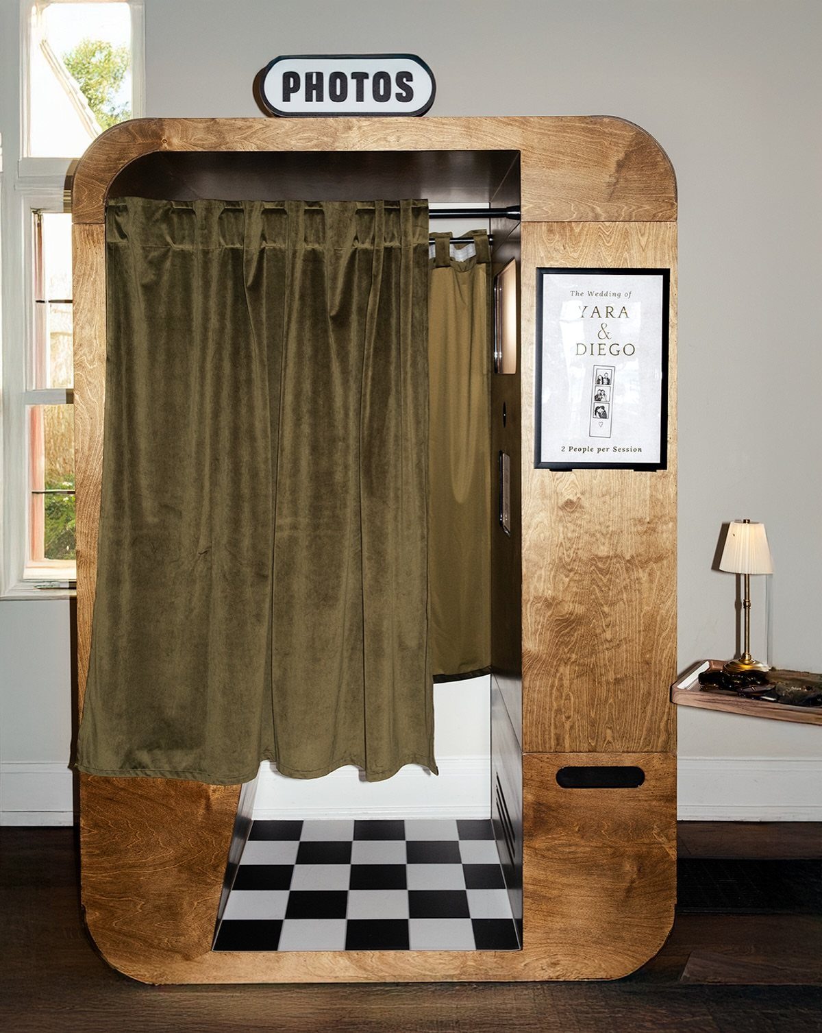 Wooden photo booth with green velvet curtains and black and white checkered flooring.