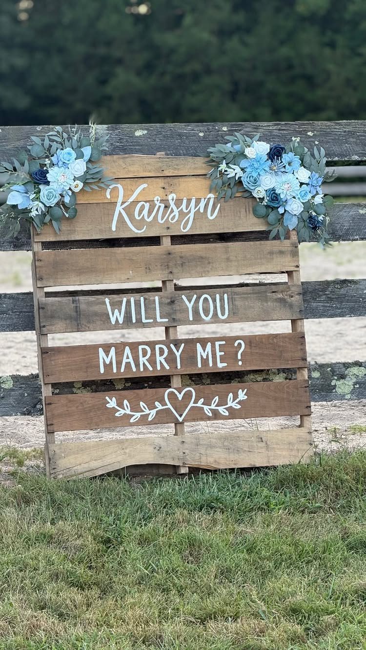 Wooden pallet proposal sign with blue flowers reading Will You Marry Me