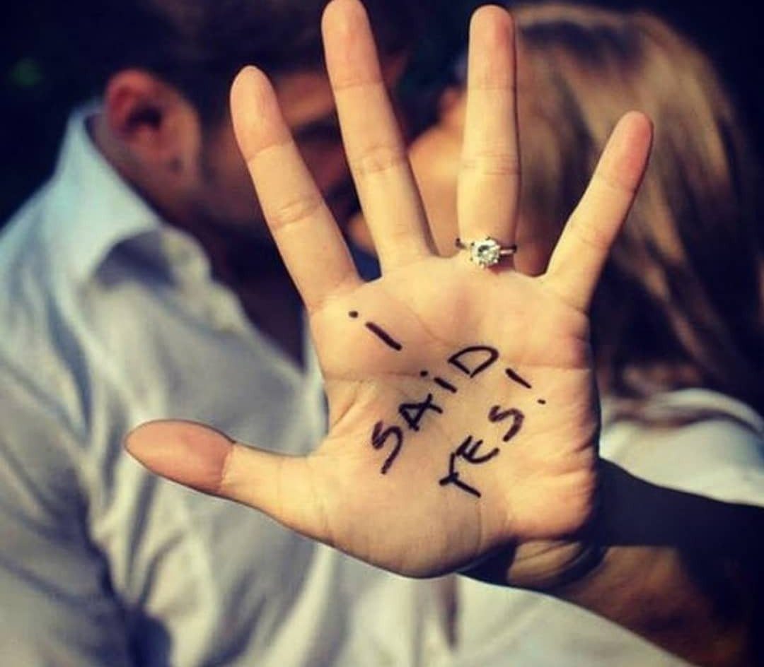 Hand with engagement ring and I SAID YES written on the palm.