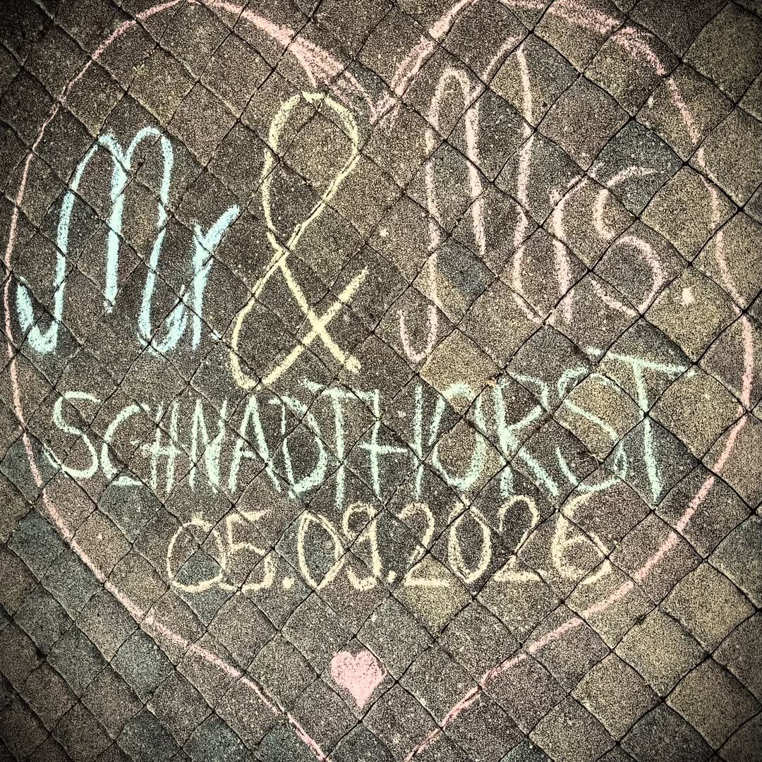 Chalk announcement on cobblestones featuring a pink heart and engagement details.