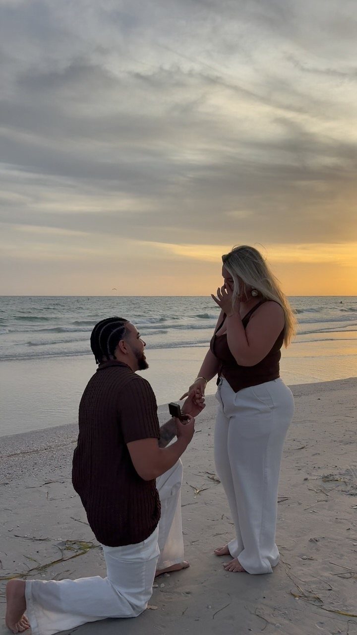 Man kneeling on a beach proposing to a woman during a golden sunset.
