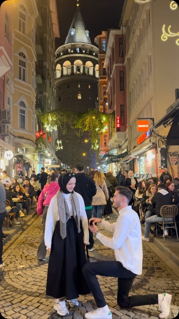 Man kneeling to propose to a woman on a cobblestone street with Galata Tower.