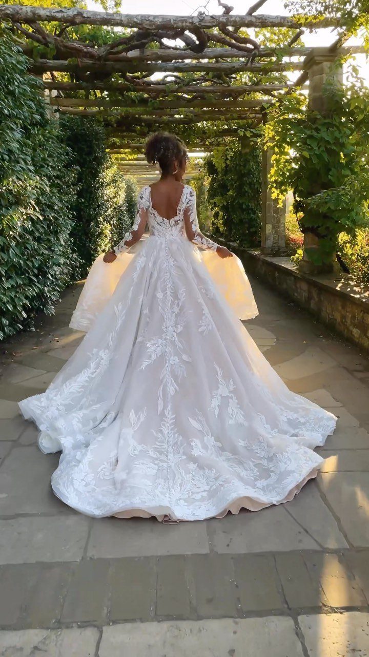Woman in a voluminous white lace bridal ball gown standing under a vine pergola