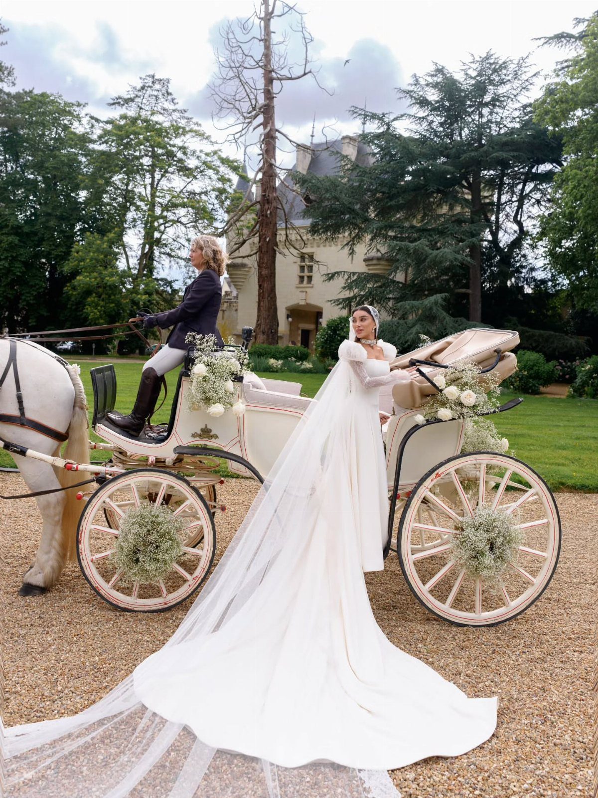 Bride in white gown standing next to a white horse-drawn wedding carriage