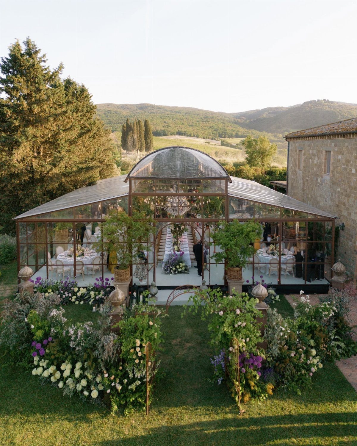 Glass conservatory wedding venue with floral decorations set against rolling green hills.