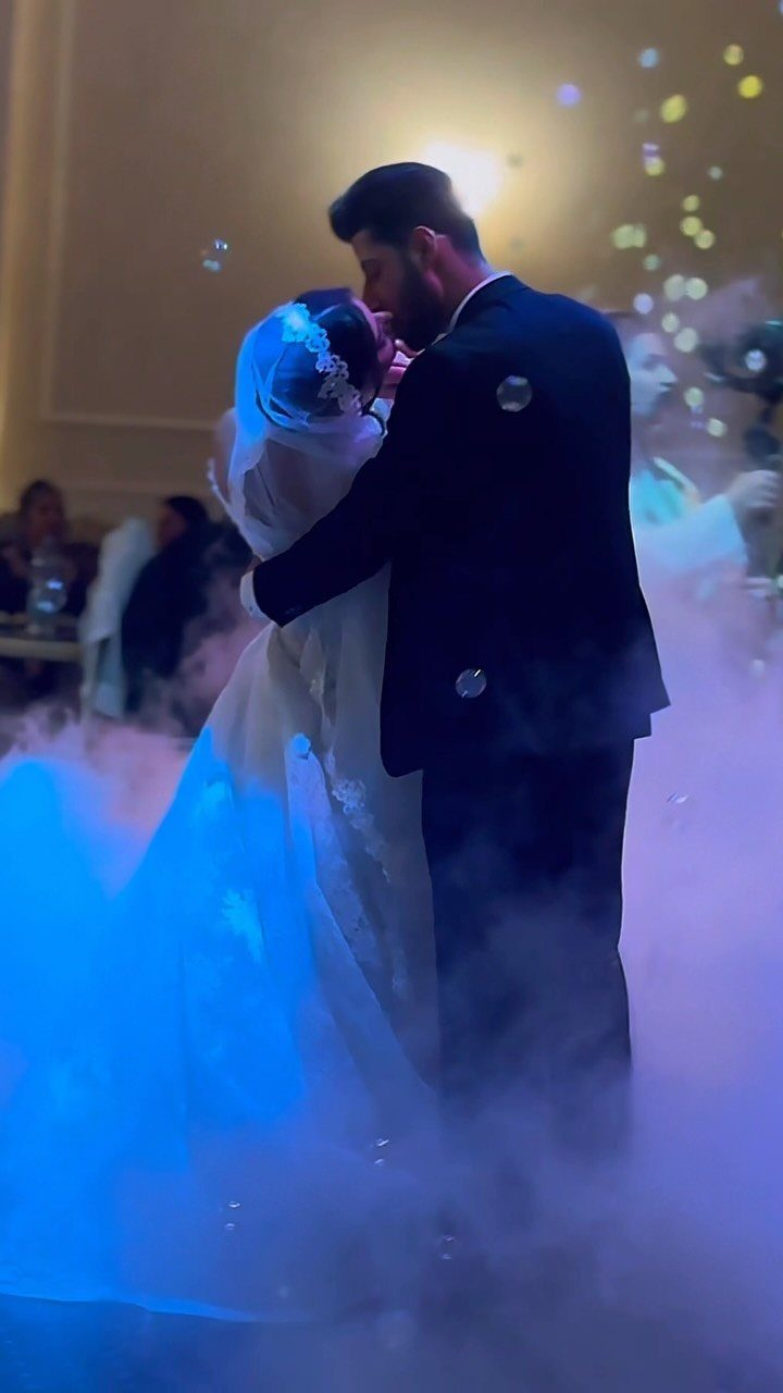 Bride and groom kissing amidst white fog and bubbles at their wedding reception.