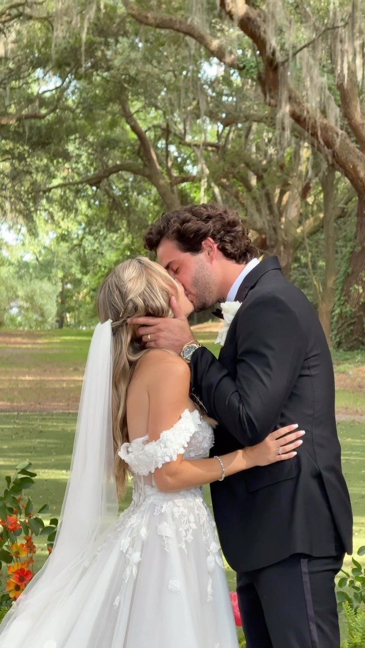 Bride and groom kissing outdoors with large mossy trees in the background.