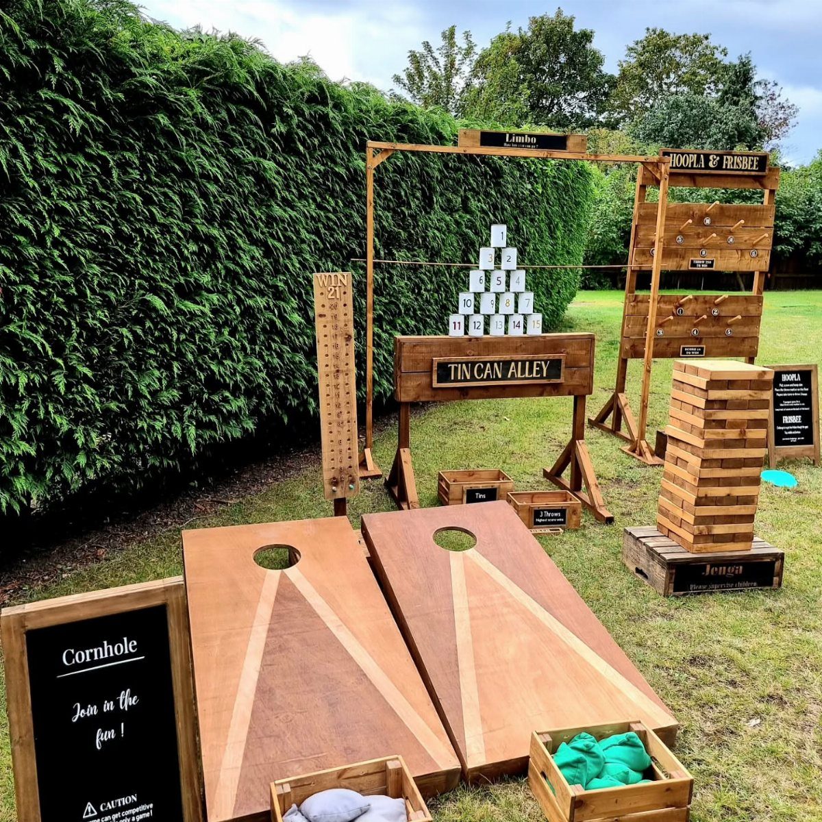 Wooden lawn games including cornhole and Jenga set up on a grassy garden lawn.