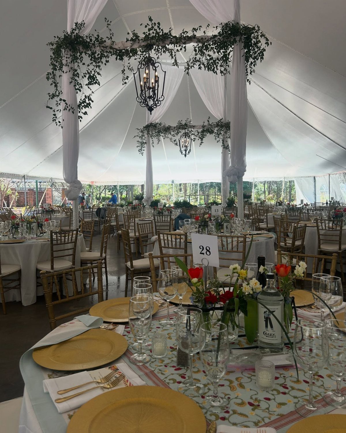 Wedding reception tables with gold chairs and greenery hanging inside a white tent.