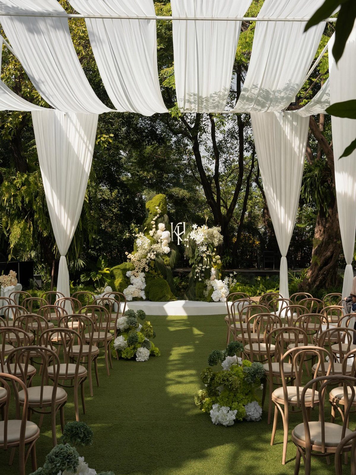 Outdoor wedding ceremony setup with white fabric draping and a greenery floral arch.