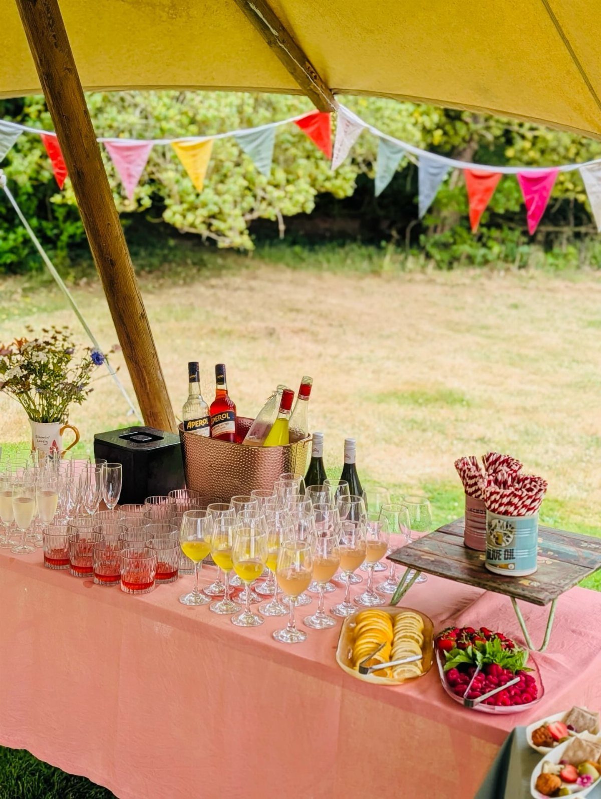 Drink station with colorful cocktails and wine under a yellow garden tent.
