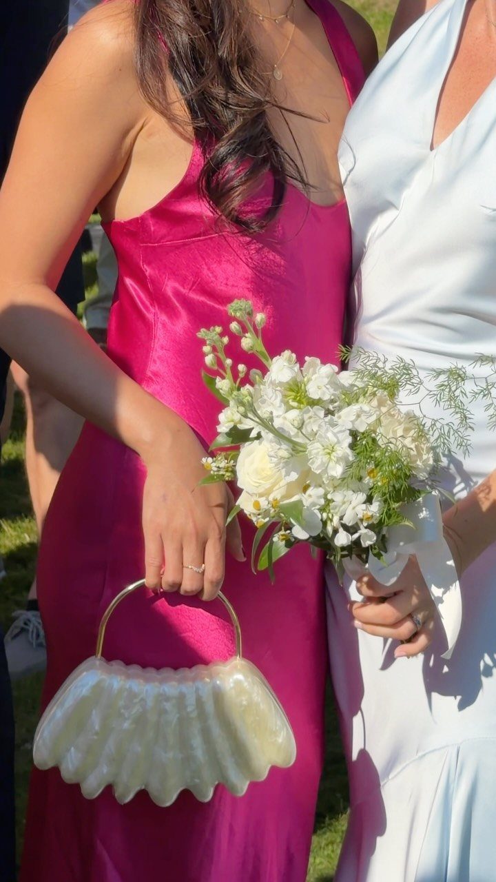Woman in pink satin dress and woman in white gown holding white flowers