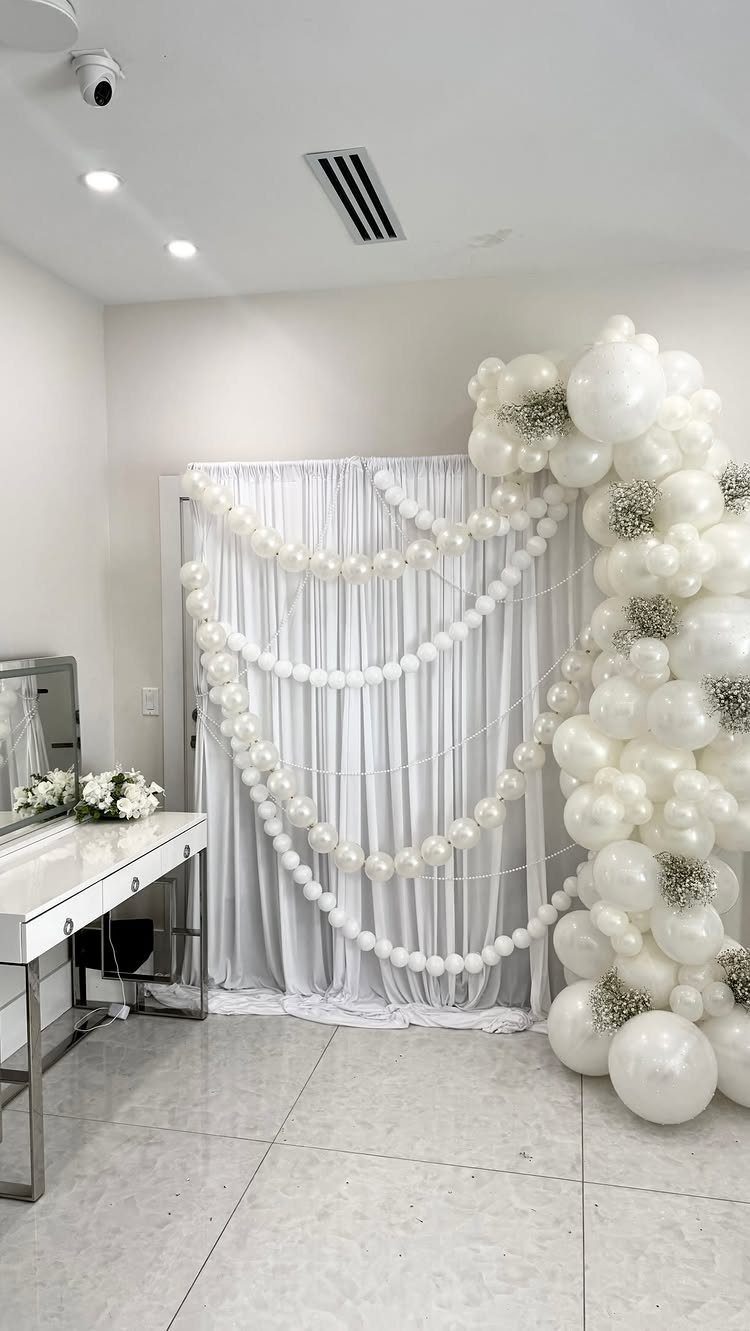 White room with a vanity table and a large white balloon arch backdrop.