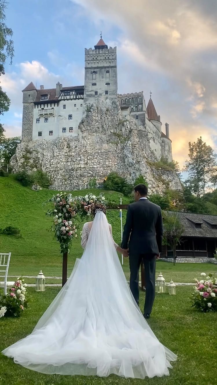 Bride and groom standing before a large white castle on a rocky cliff
