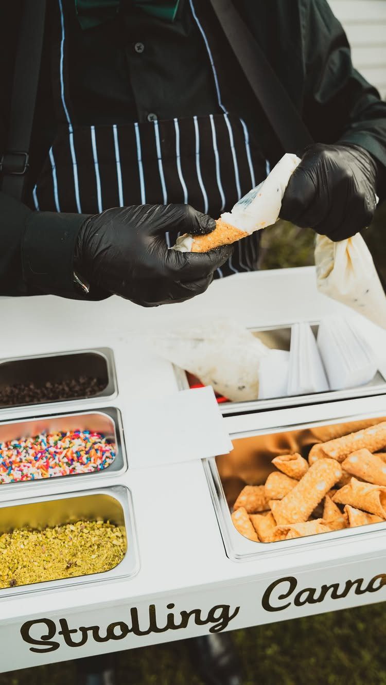 Food vendor in black gloves preparing fried pastries at a white catering station