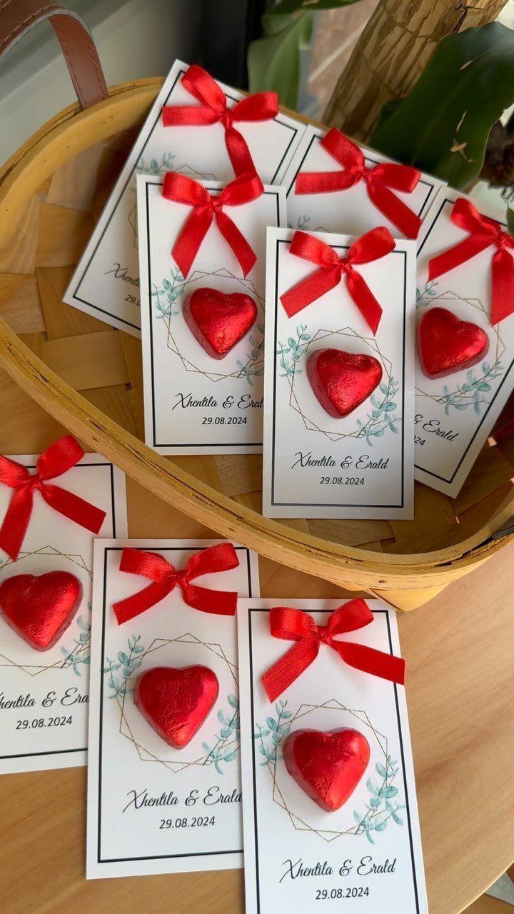 Heart-shaped chocolates with red bows on personalized wedding favor cards in a basket