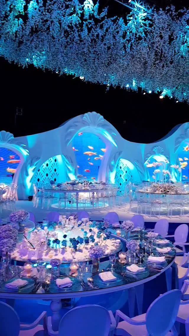 Underwater themed event decor with blue lighting, shell structures, and elegant table settings.