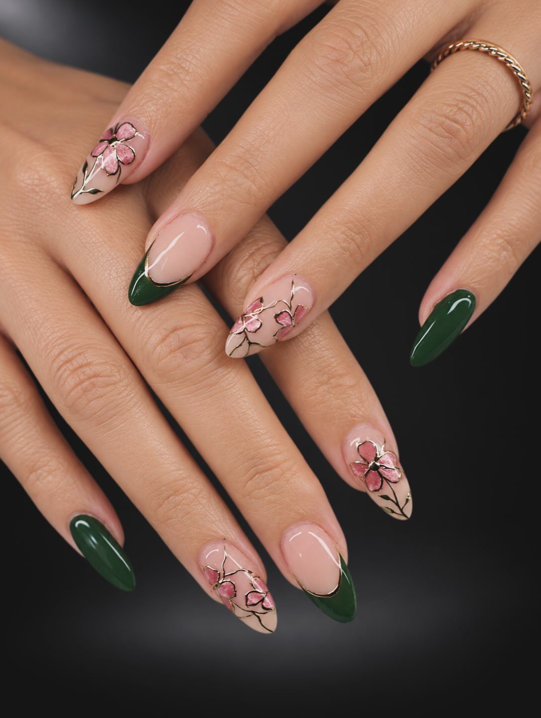 Almond-shaped nails with deep green polish and pink floral art with gold accents.