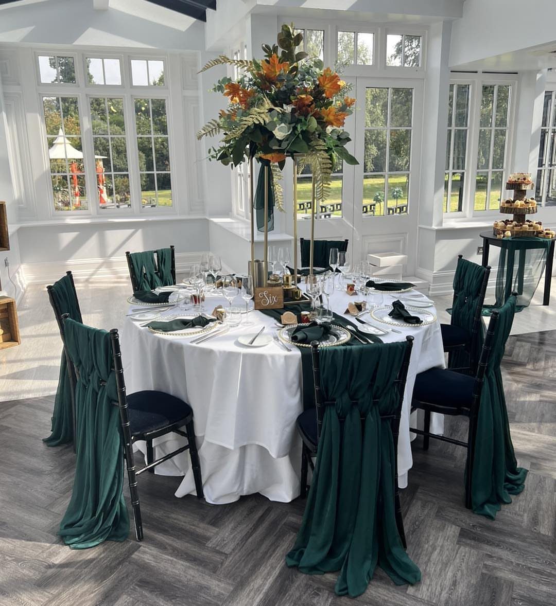 Wedding table with white linens, emerald green chair sashes, and autumn floral centerpiece.