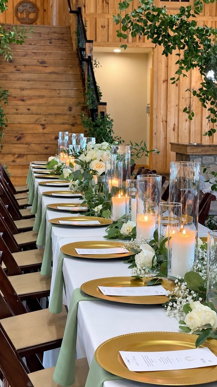 Wedding table with sage green runners, gold plates, and white floral candle centerpieces.