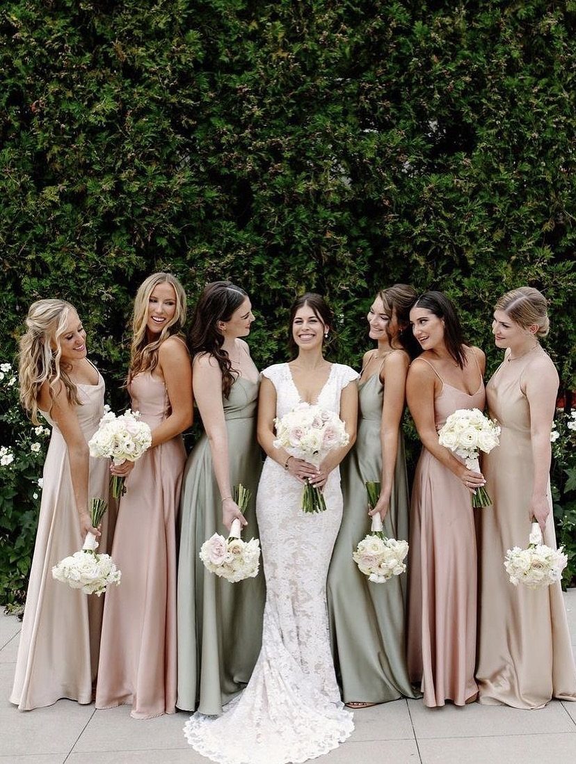 Bride and bridesmaids in sage and mauve dresses holding white floral bouquets.