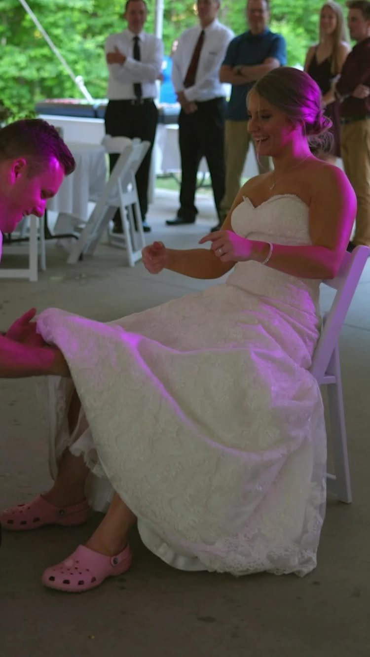 Bride in white wedding dress wearing pink Crocs while groom reaches for garter