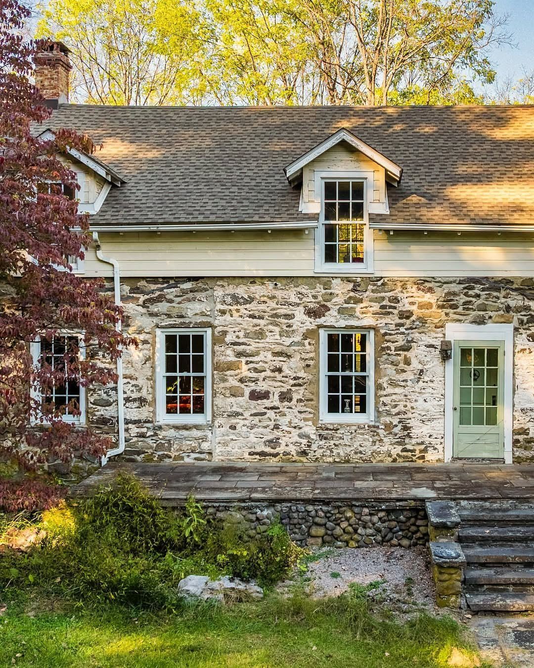 Stone cottage with white windows and green door surrounded by autumn foliage