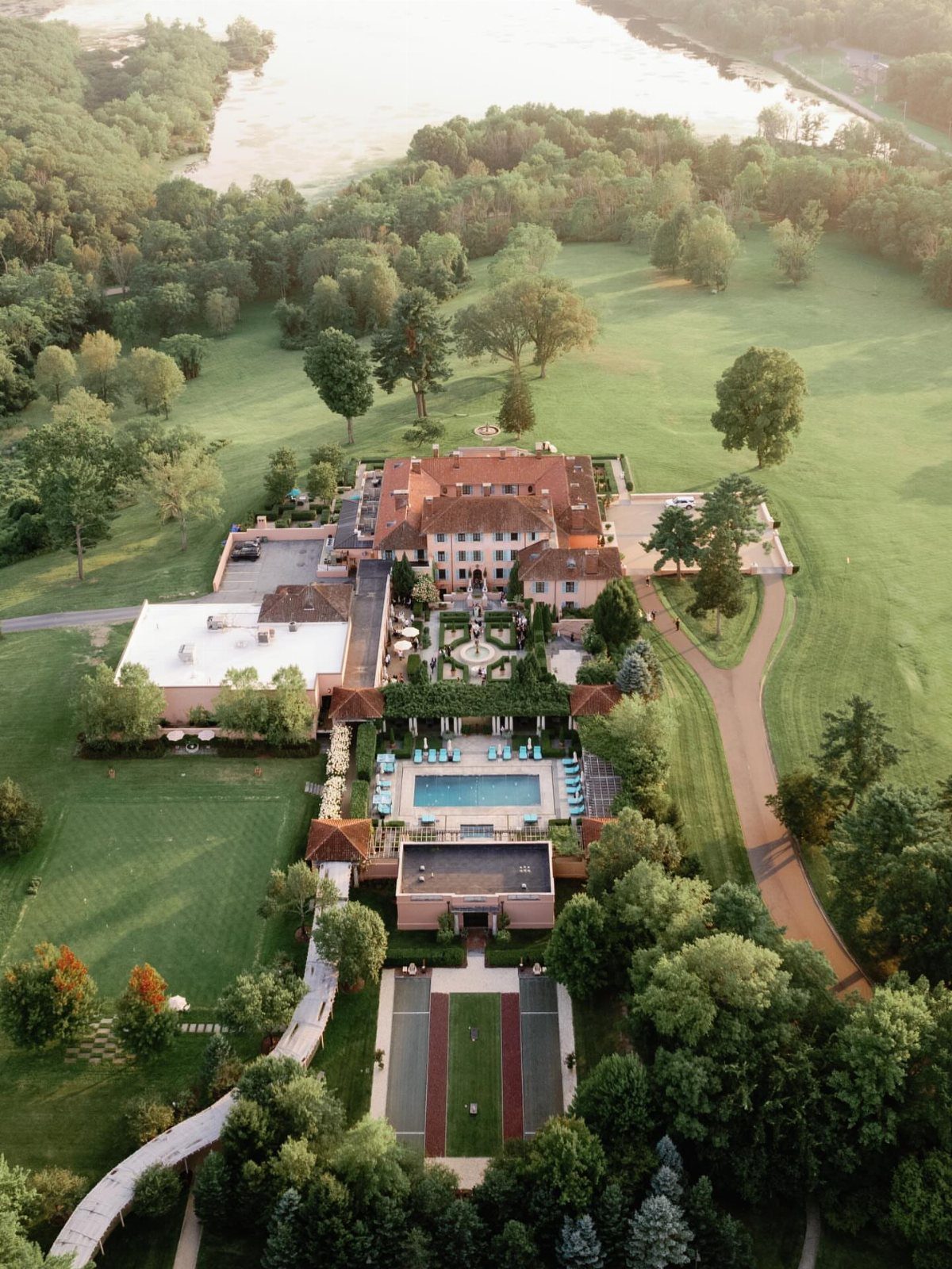 Historic estate with red-tiled roof, swimming pool, and gardens near a river.