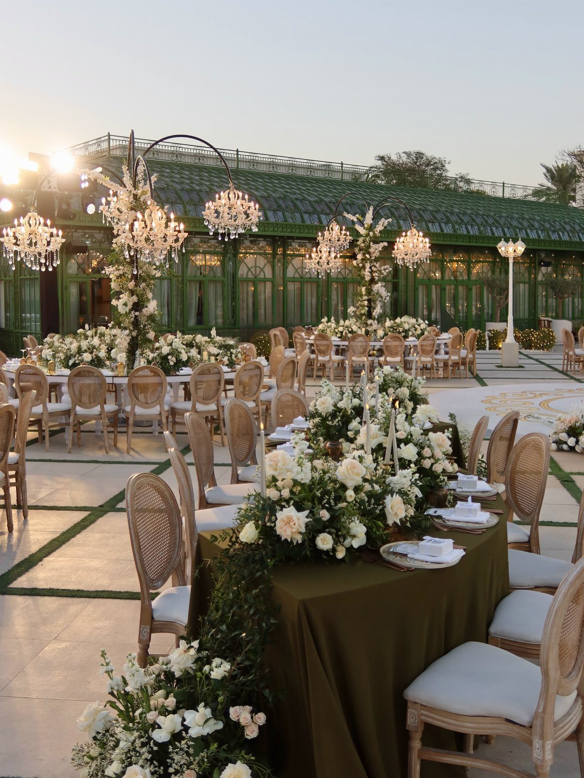 Outdoor wedding reception with olive green tables, white flowers, and hanging crystal chandeliers.