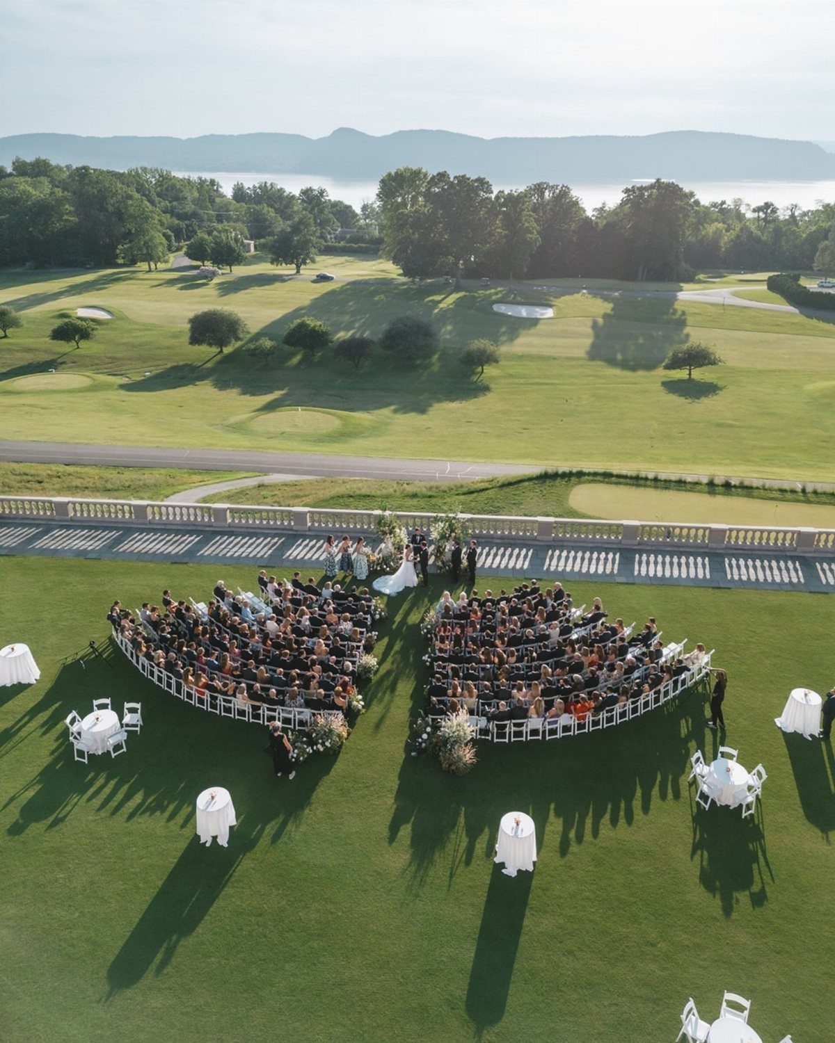 Outdoor wedding ceremony with curved white seating overlooking a lush golf course and mountains.