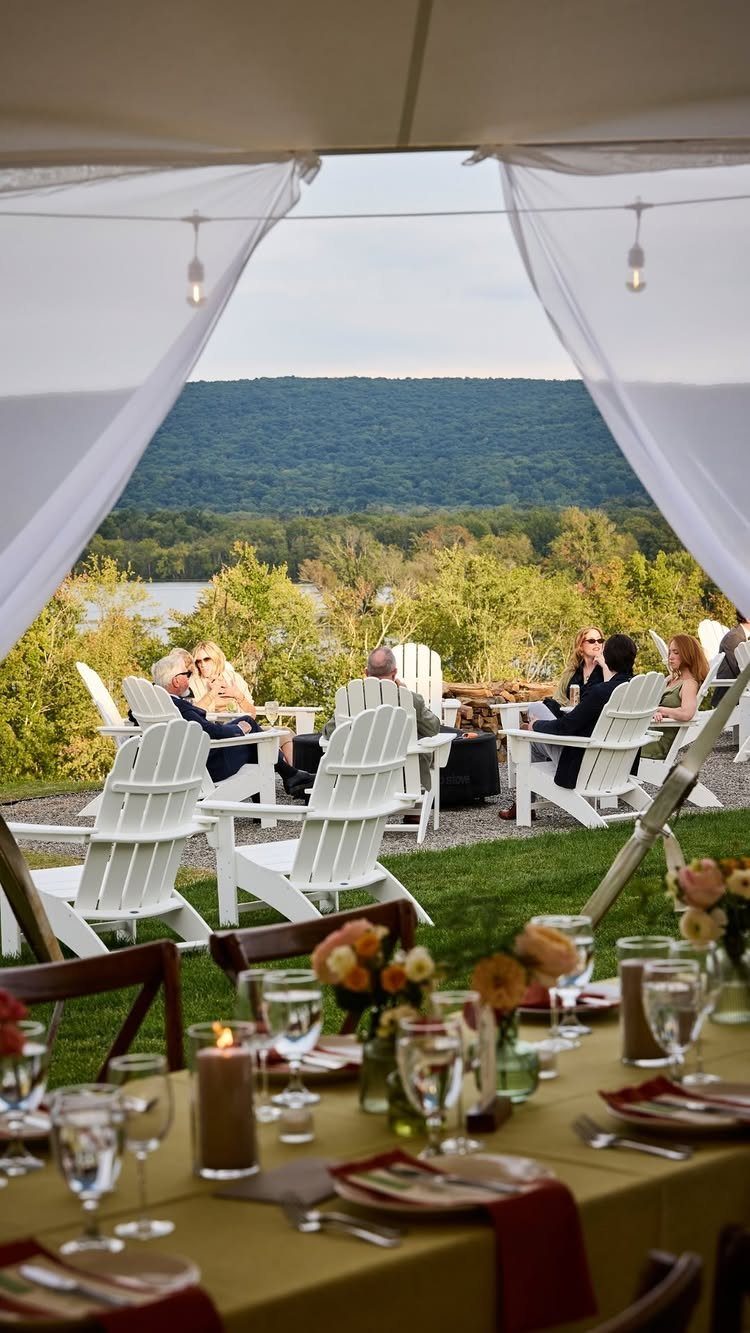 Dining table and guests in Adirondack chairs overlooking a river and mountains.