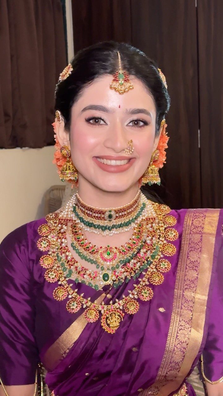 Woman in purple saree wearing ornate gold and emerald bridal jewellery sets