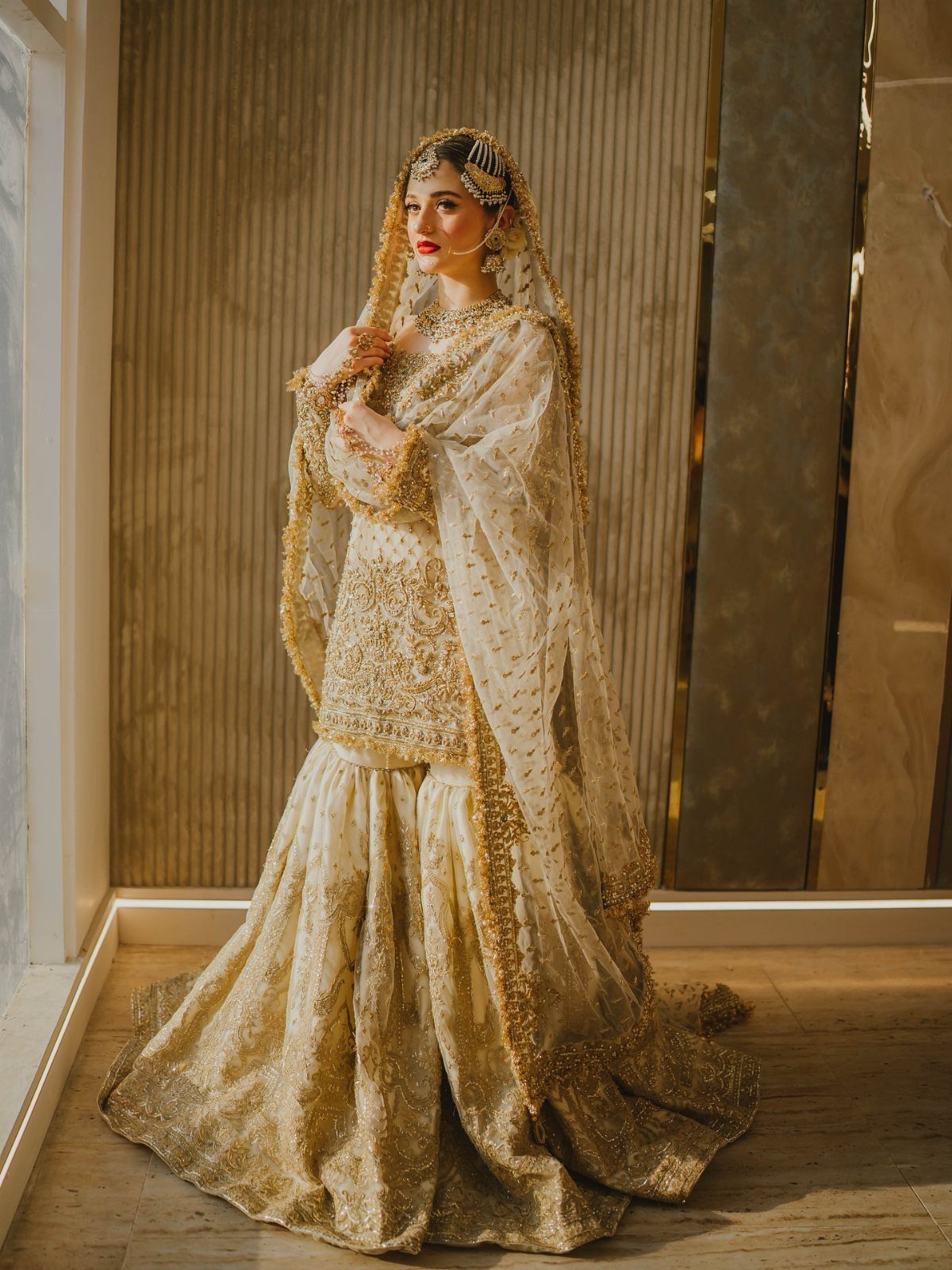 Woman in gold embroidered gharara set with traditional bridal jewelry and dupatta