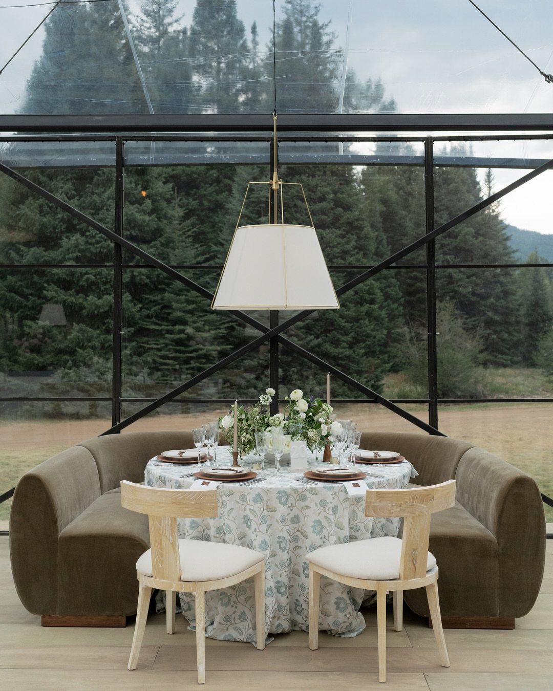 Elegant wedding table setting inside a glass pavilion overlooking a mountain pine forest.