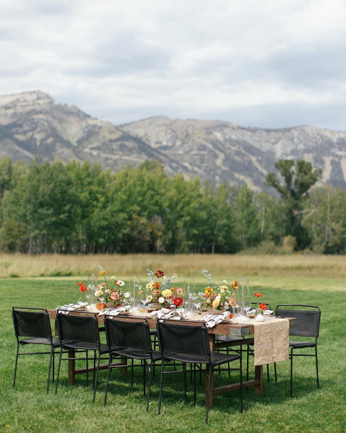 Outdoor dining table with floral arrangements set against a backdrop of mountains and trees.