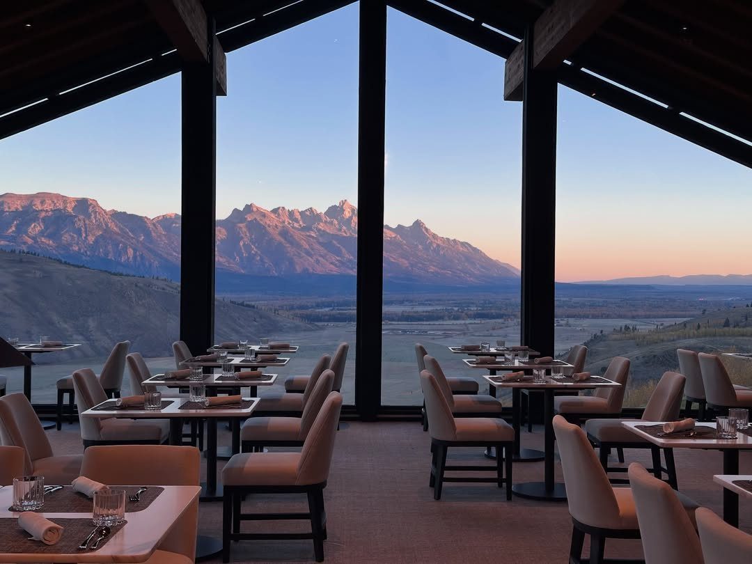 Dining room with set tables overlooking the Teton mountain range at sunset.