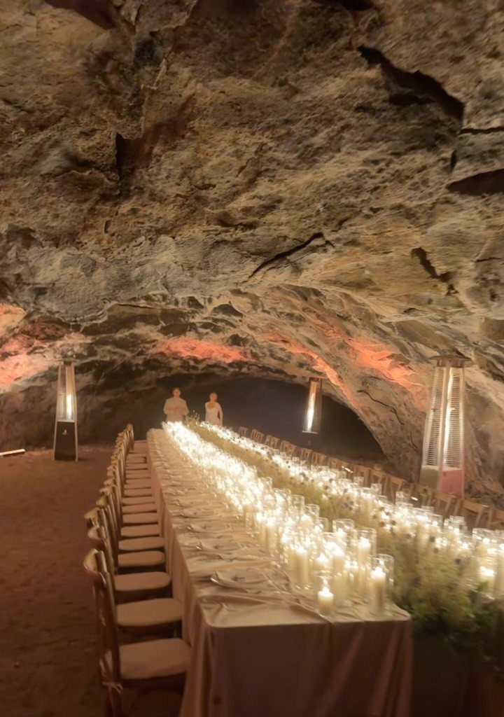 Long candlelit dining table set inside a large rocky cave for a wedding reception