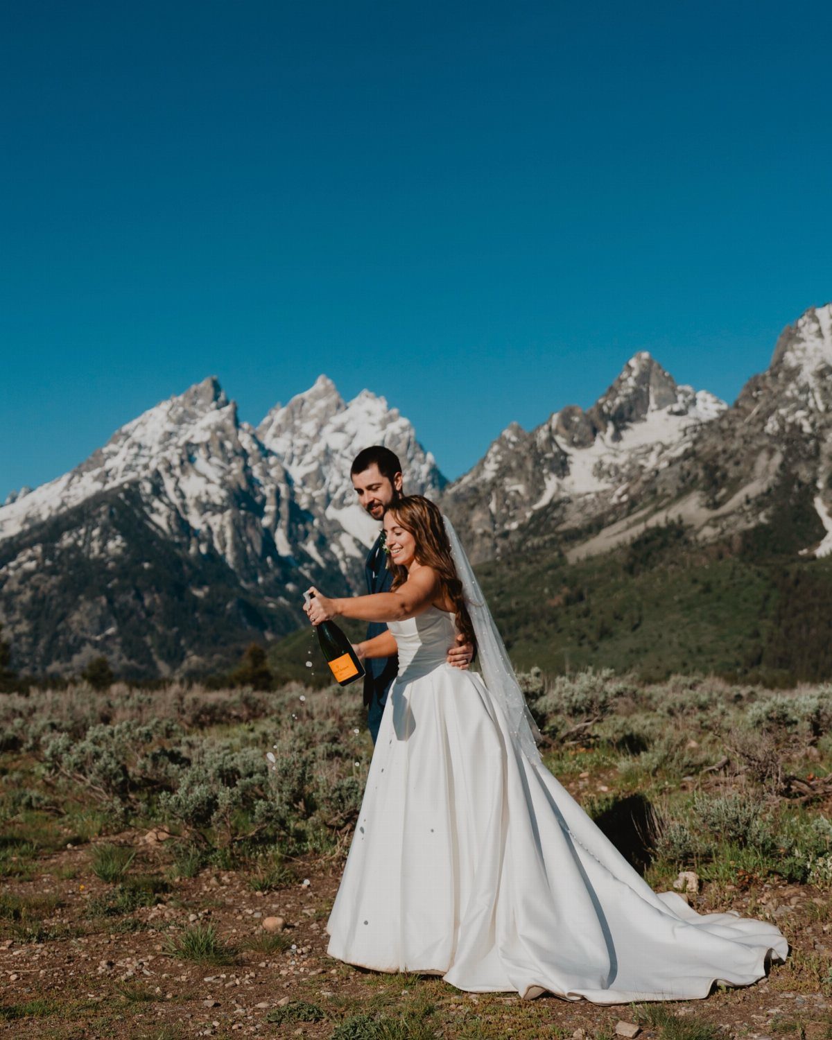 Bride and groom popping champagne with snow-capped mountains in the background.