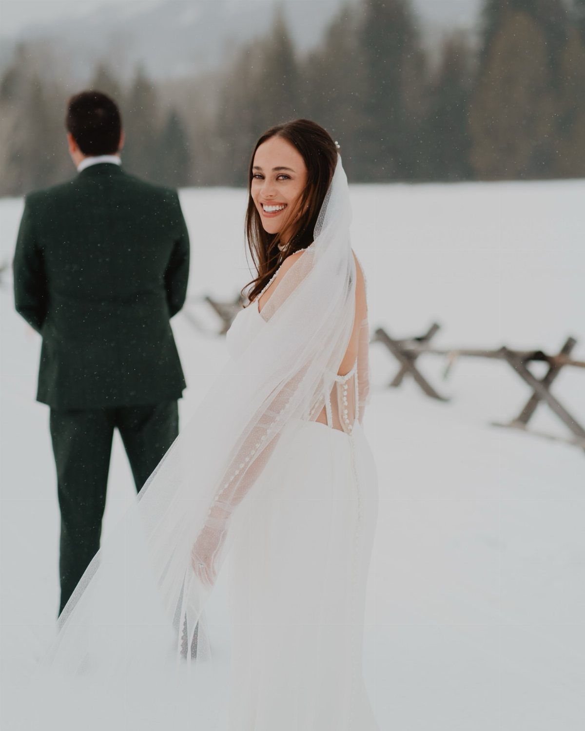 Bride in white dress and groom in green suit in snowy mountain landscape