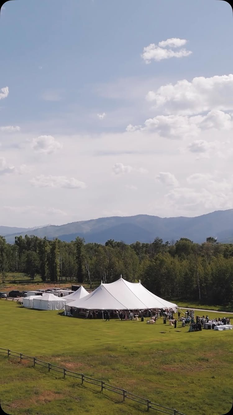 Large white wedding tent on a green field with mountains in the background
