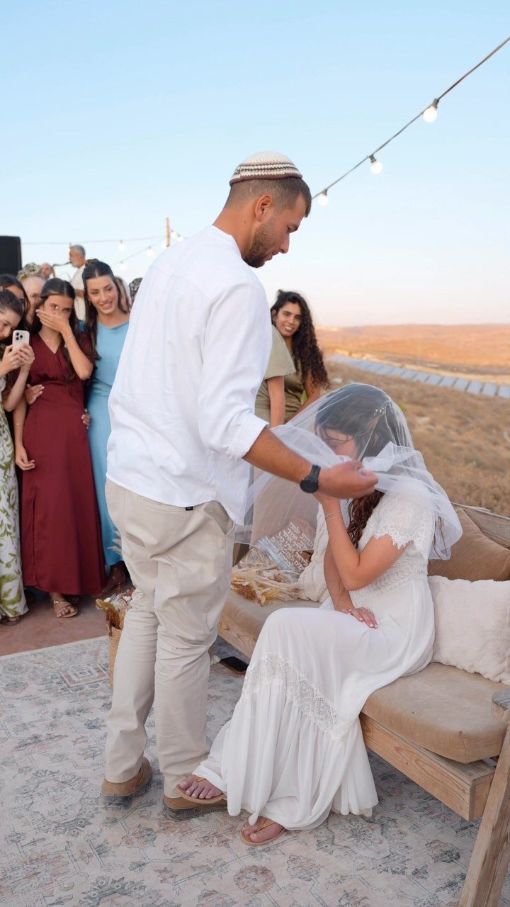 Groom placing a white veil over a bride's face during a wedding ceremony.