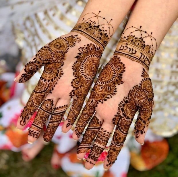 Hands with intricate brown henna designs and Hebrew text on the wrist.